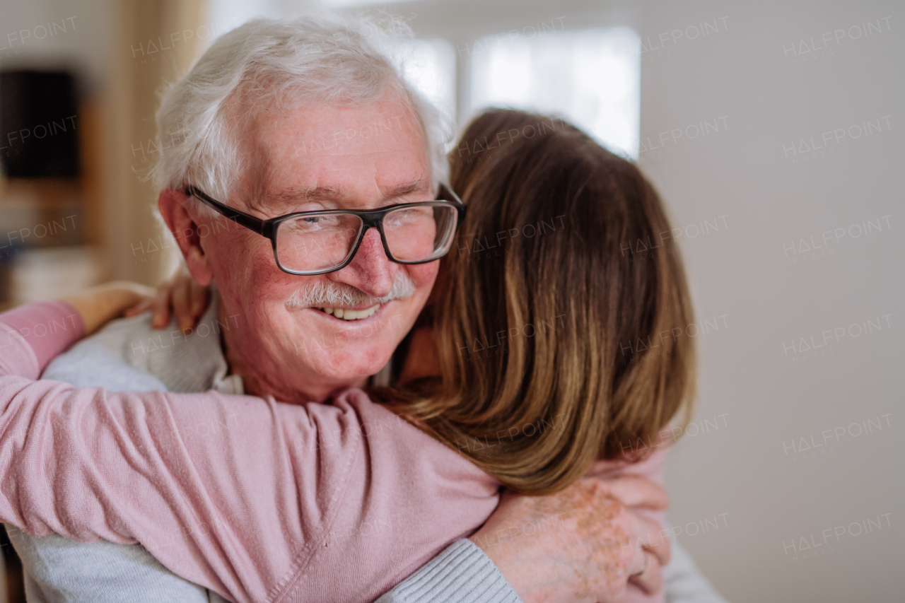 A rear view of adult daughter hugging her senior father when visitng him at home.