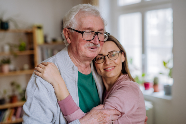 An adult daughter hugging her senior father when visitng him at home.