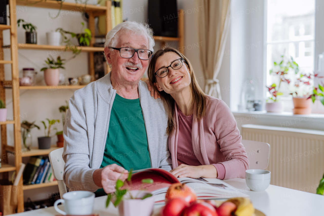 An adult daughter visiting her senior father at home and having coffee together, looking at book.