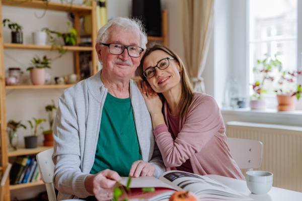 An adult daughter visiting her senior father at home and having coffee together, looking at book.