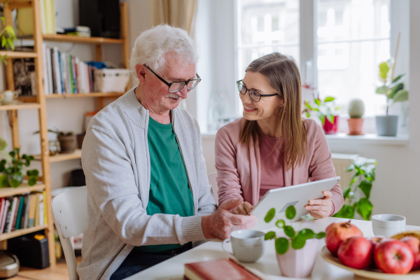 An adult daughter visiting her senior father at home and using tablet.