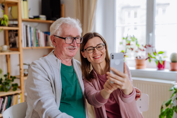 An adult daughter visiting her senior father at home and taking selfie.