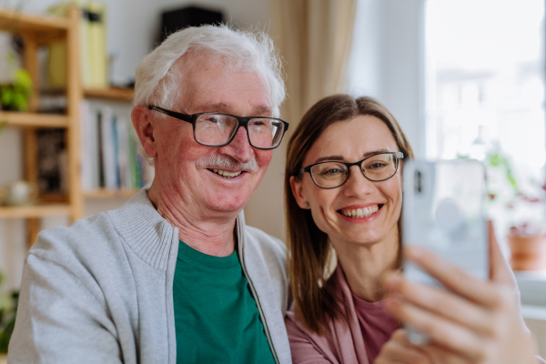 An adult daughter visiting her senior father at home and taking selfie.