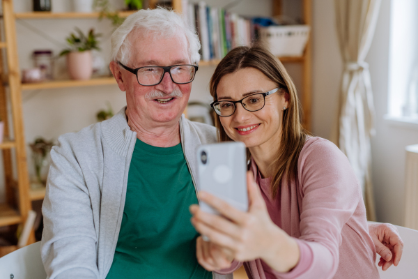 An adult daughter visiting her senior father at home and taking selfie.