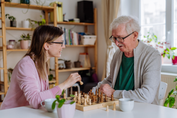 An adult daughter visiting her senior father at home and playing chess together.