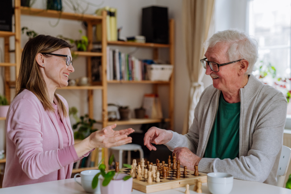 An adult daughter visiting her senior father at home and playing chess together.