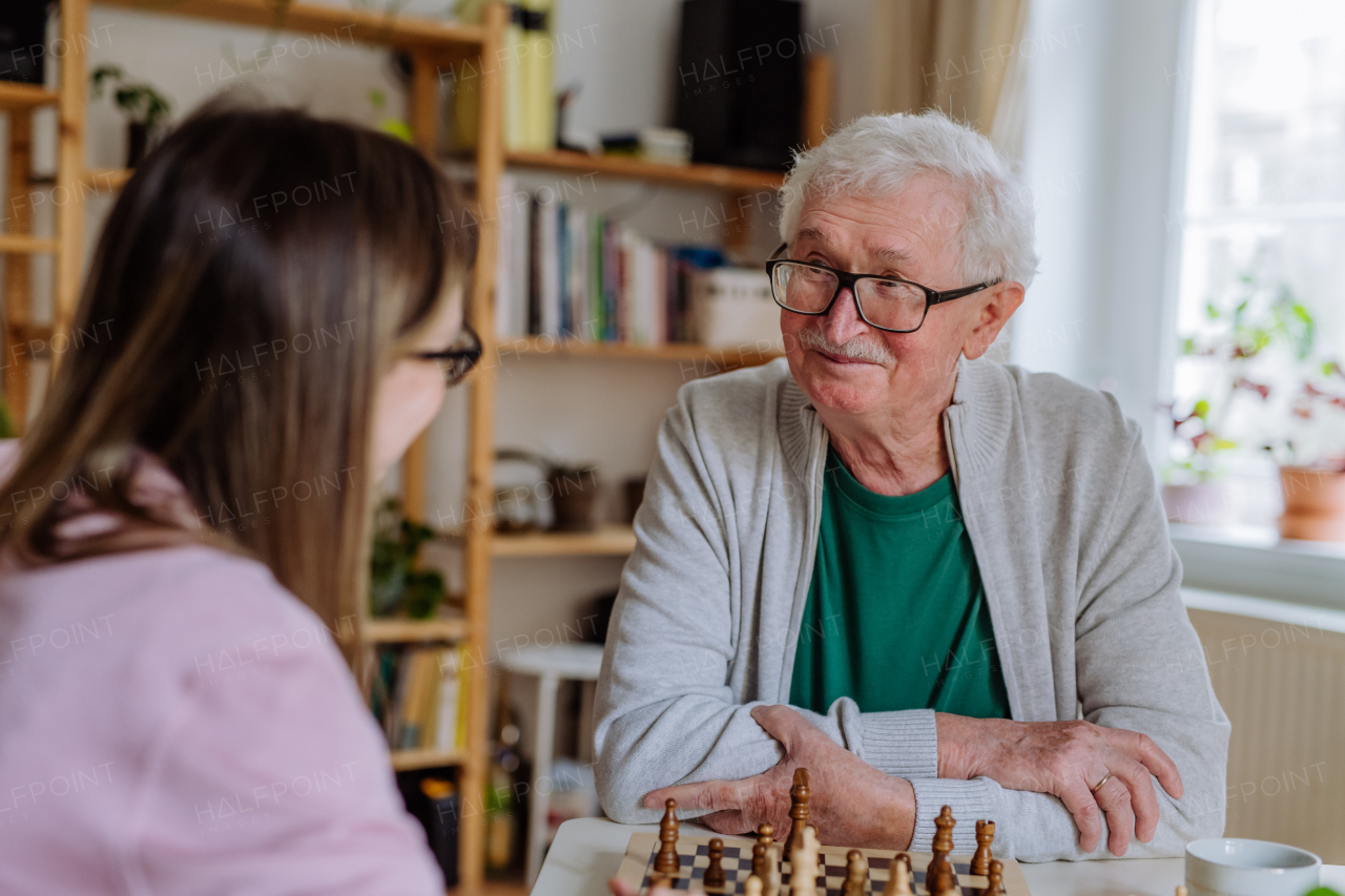 An adult daughter visiting her senior father at home and playing chess together.