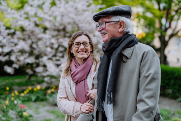 A happy senior man with adult daughter outdoors on a walk in park.