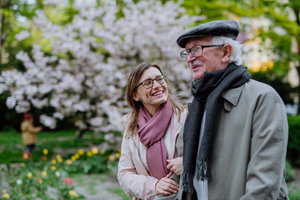 A happy senior man with adult daughter outdoors on a walk in park.