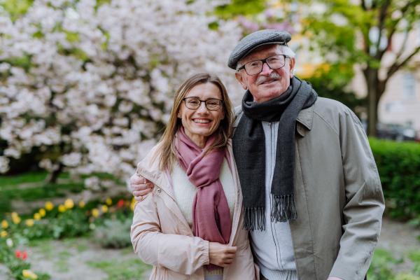 An adult daughter hugging her senior father outdoors in park on spring day.