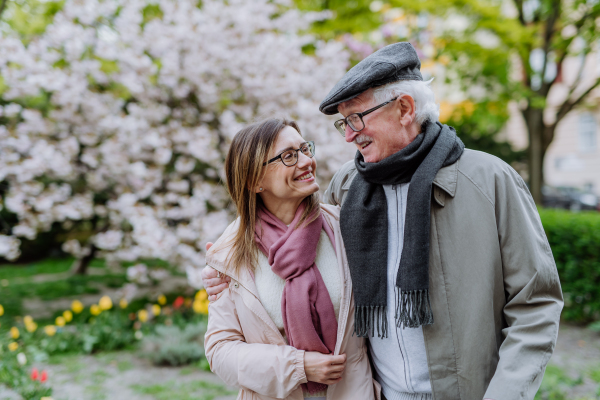 A happy senior man with adult daughter outdoors on a walk in park.