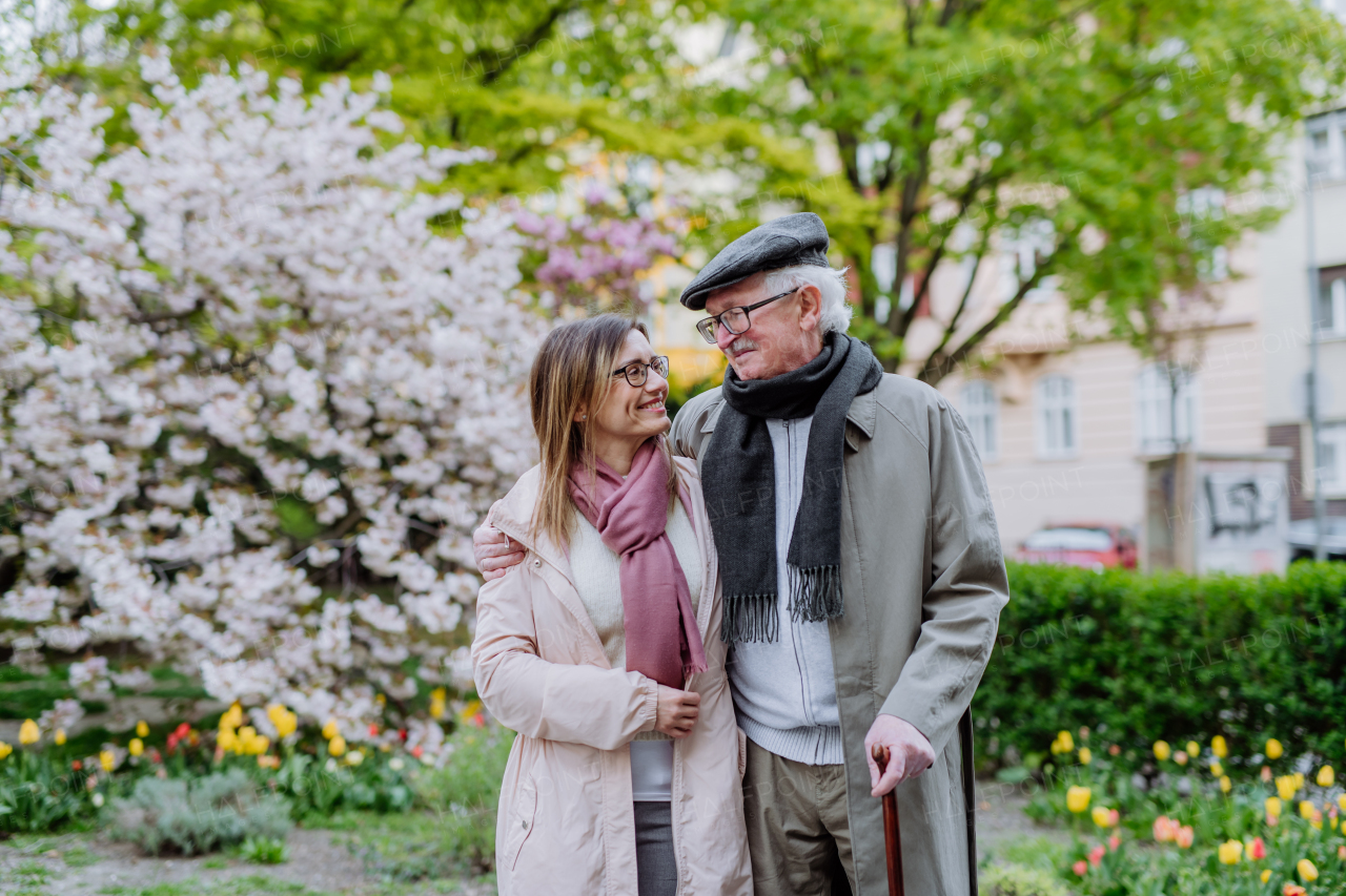 A happy senior man with walking stick and adult daughter outdoors on a walk in park.