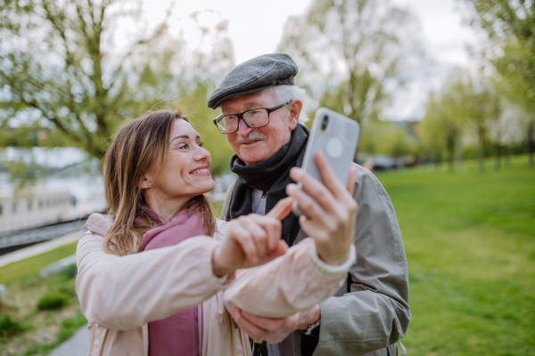 A happy senior man and his adult daughter taking selfie outdoors on a walk in park.