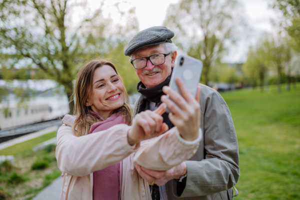 A happy senior man and his adult daughter taking selfie outdoors on a walk in park.