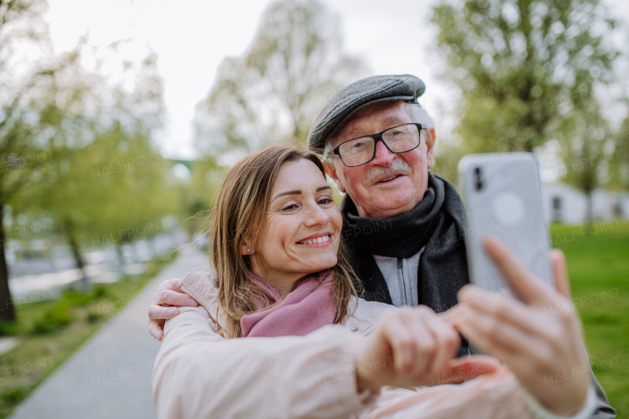 A happy senior man and his adult daughter taking selfie outdoors on a walk in park.