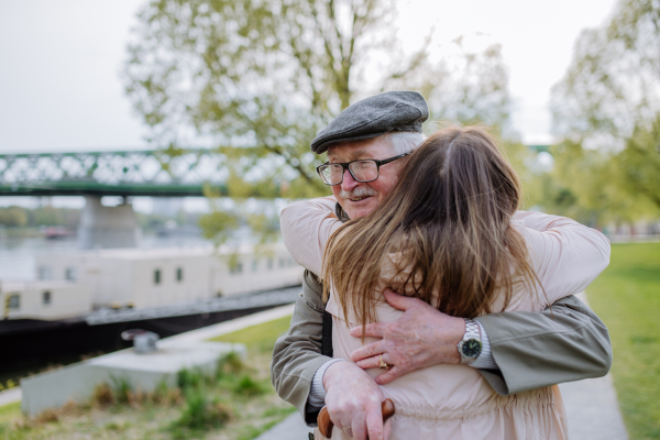 A rear view of adult daughter hugging her senior father when meeting him outdoors in street.