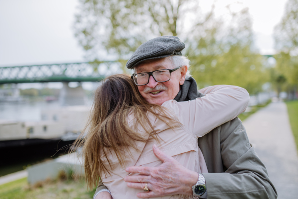 A rear view of adult daughter hugging her senior father when meeting him outdoors in street.