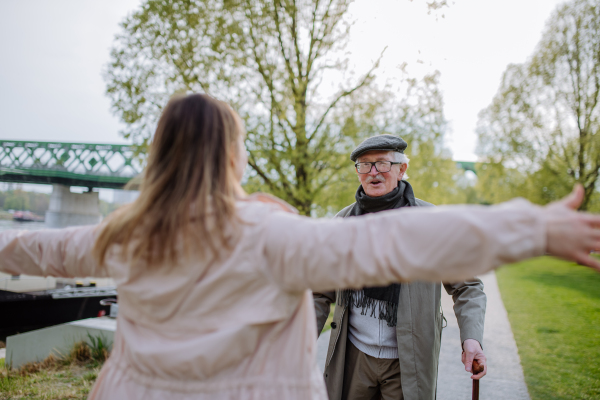 A rear view of adult daughter hugging her senior father when meeting him outdoors in street.