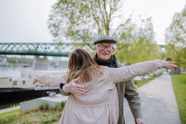 A rear view of adult daughter hugging her senior father when meeting him outdoors in street.