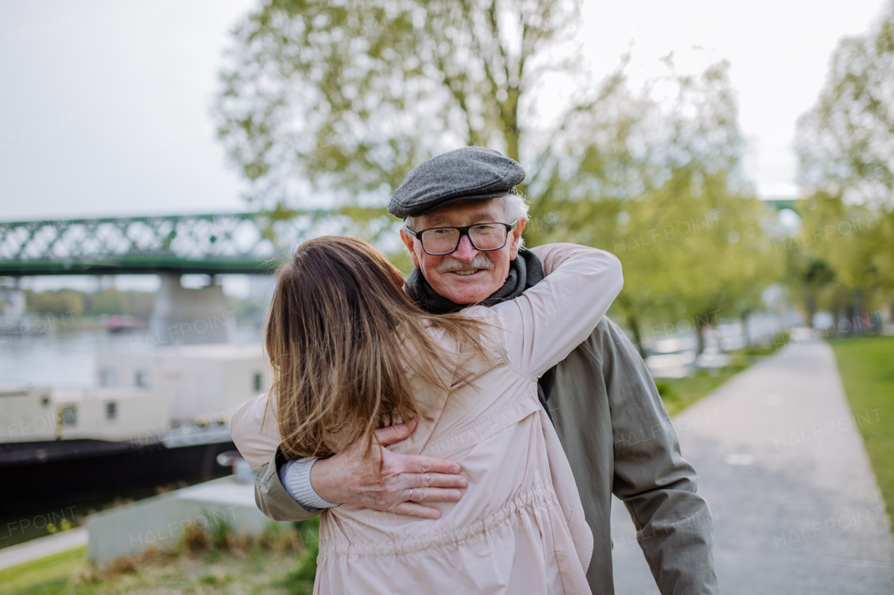 A rear view of adult daughter hugging her senior father when meeting him outdoors in street.