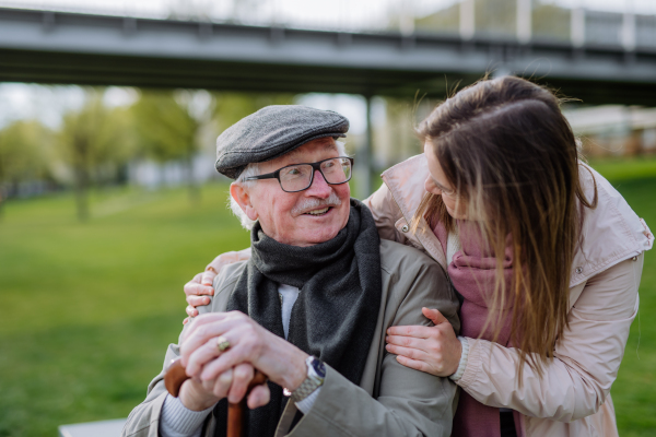 A happy senior with his adult daughter sitting outdoors in park.