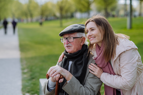 A happy senior with his adult daughter sitting outdoors in park.