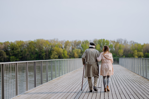 A rear view of senior man with daughter outdoors on a walk on pier by river.