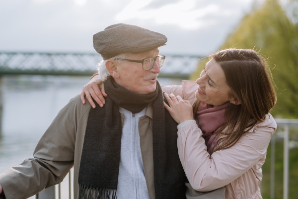 An adult daughter hugging her senior father outdoors in park on spring day.