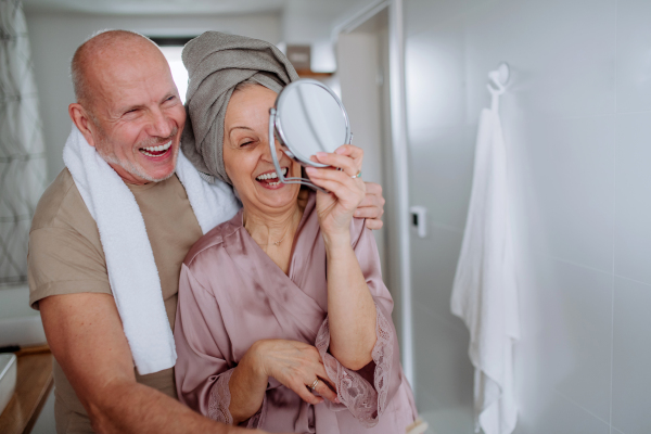 A senior couple in love in bathroom, looking at mirror and smiling, morning routine concept.