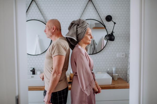 A senior couple in bathroom, standing back to back, relationship problems concept.