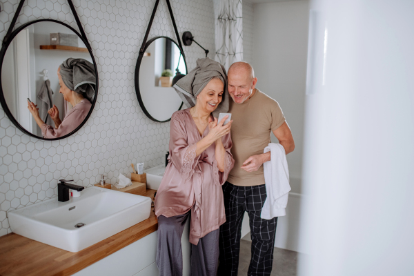 A senior couple in love in bathroom, using smartphone, morning routine concept.