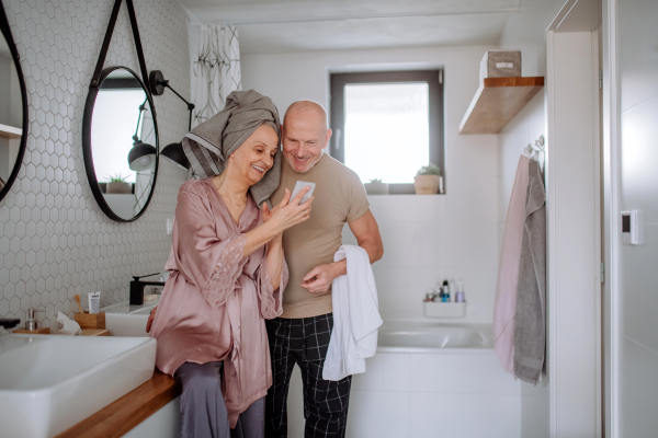 A senior couple in love in bathroom, using smartphone, morning routine concept.