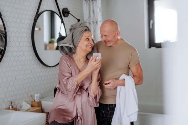 A senior couple in bathroom, using telephone, talking and having fun, morning routine concept.