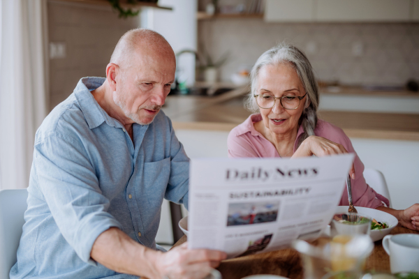 A happy senior couple having breakfast and reading newspaper together at home.