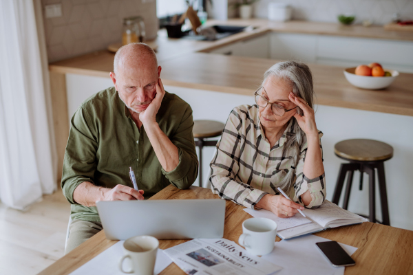 A stressed senior couple calculate expenses or planning budget together at home.