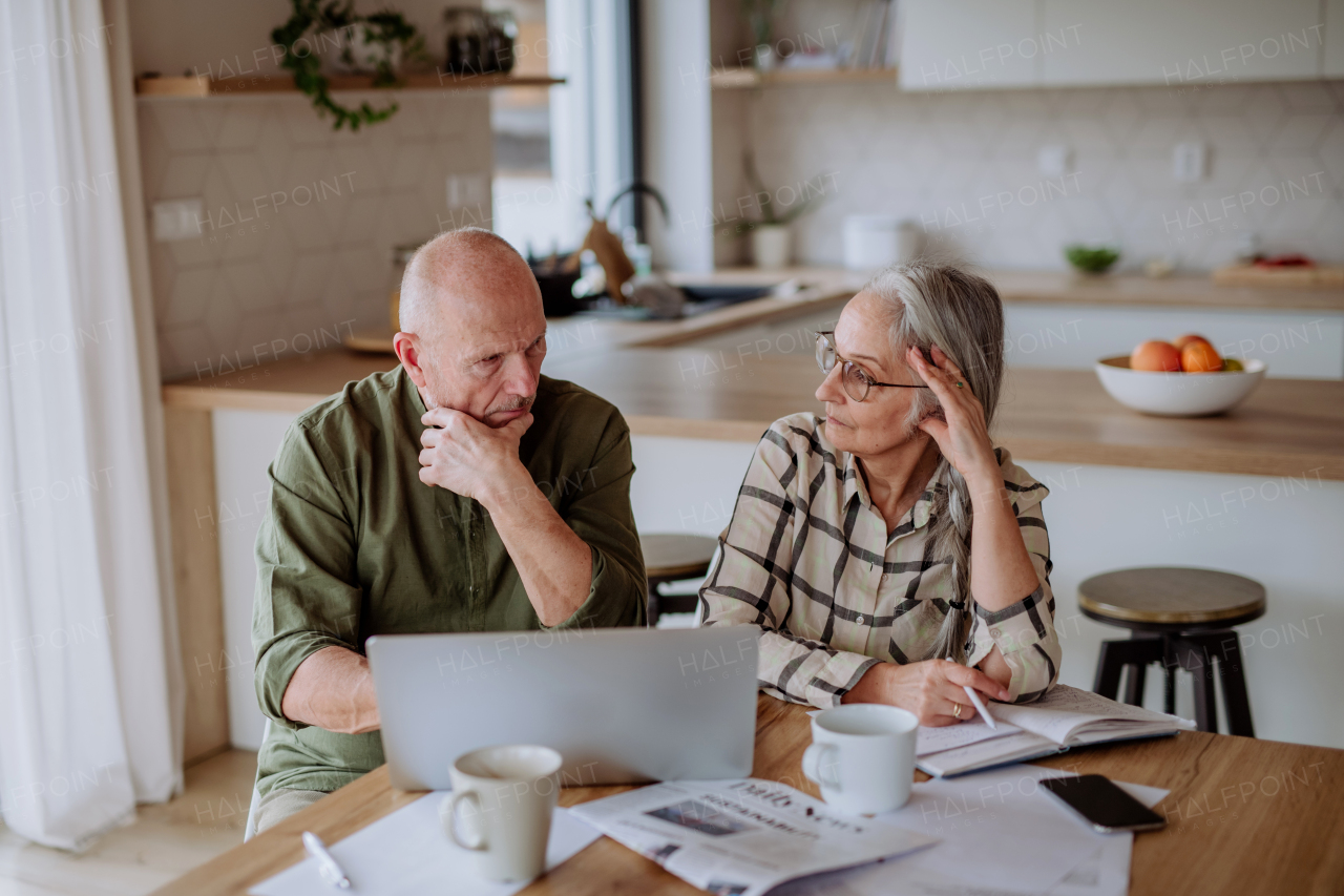 A stressed and sad senior couple calculate expenses or planning budget together at home.