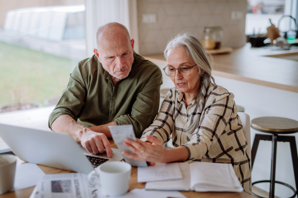 A stressed senior couple calculate expenses or planning budget together at home.