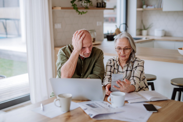 A stressed senior couple calculate expenses or planning budget together at home.