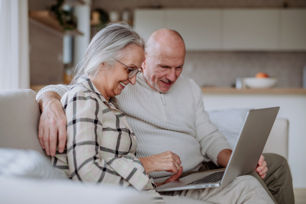 Cheerfull senior couple sitting on sofa and using laptop together.