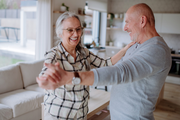 A cheerful senior couple dancing together at home.