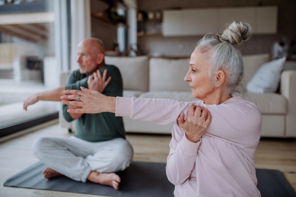 A senior couple doing relaxation exercise together at home.