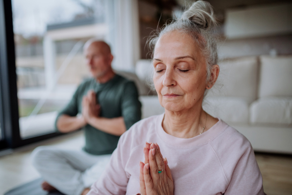 A senior couple doing relaxation exercise together at home.