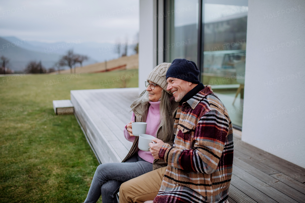 A happy senior couple sitting on terrace and drinking coffee together.