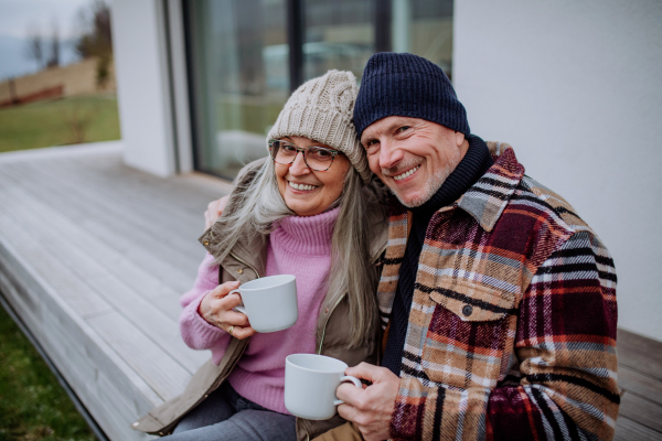 A happy senior couple sitting on terrace and drinking coffee together.