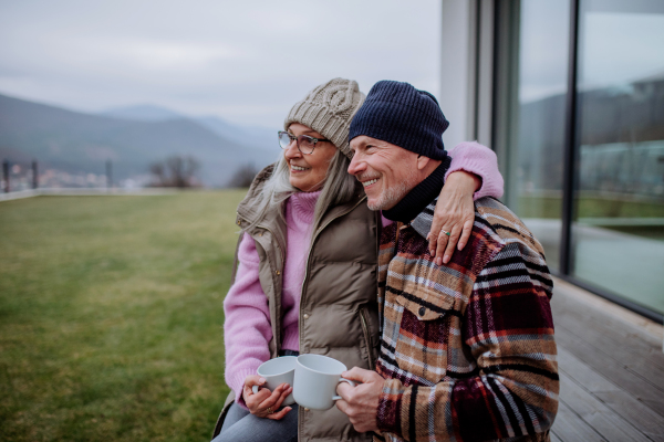 A happy senior couple sitting on terrace and drinking coffee together.