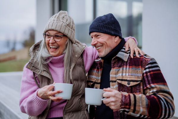 A happy senior couple sitting on terrace and drinking coffee together.