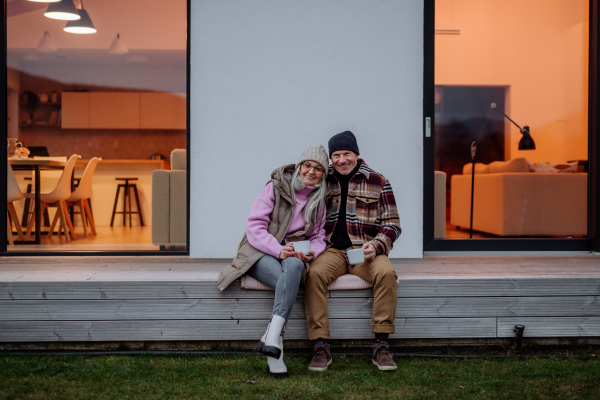 A happy senior couple sitting on terrace and drinking coffee together.