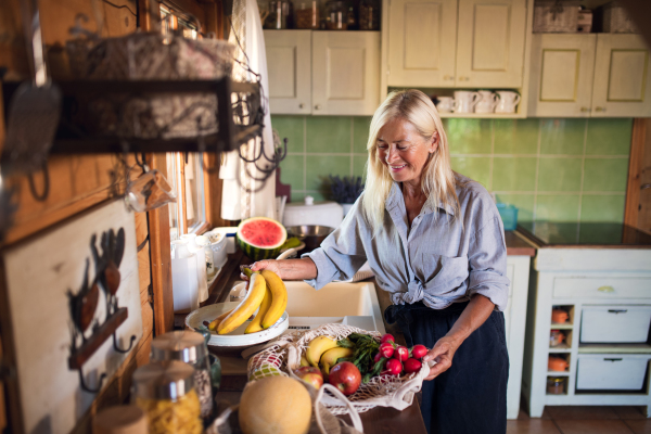 A happy senior woman unpacking shopping indoors at home, sustainable lifestyle.