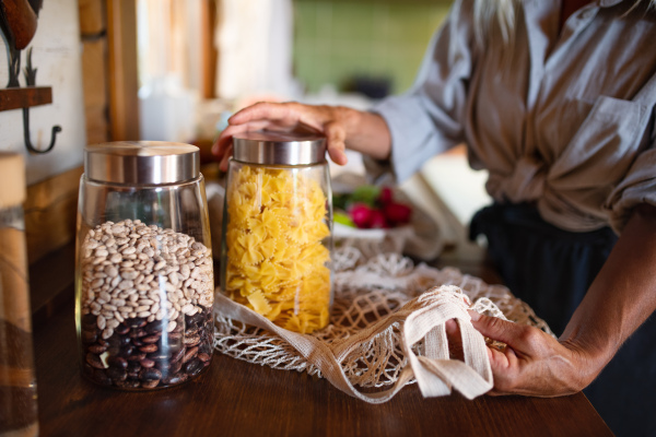 A close-up of senior woman unpacking local food in zero waste packaging from bag in kitchen at home.