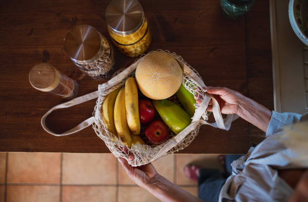 A top view of senior woman unpacking local food in zero waste packaging from bag in kitchen at home.